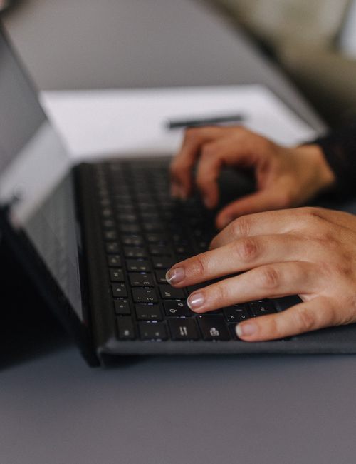 Detailaufnahme: Hände einer Mitarbeiterin tippen auf Laptop-Tastatur im Arbeitsalltag